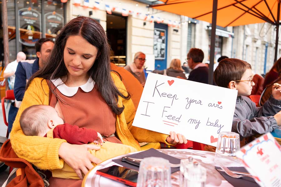 Une maman allaitant son bébé, avec une pancarte Keep your avis, I feed my baby, lors de JFJM 2025 Bordeaux