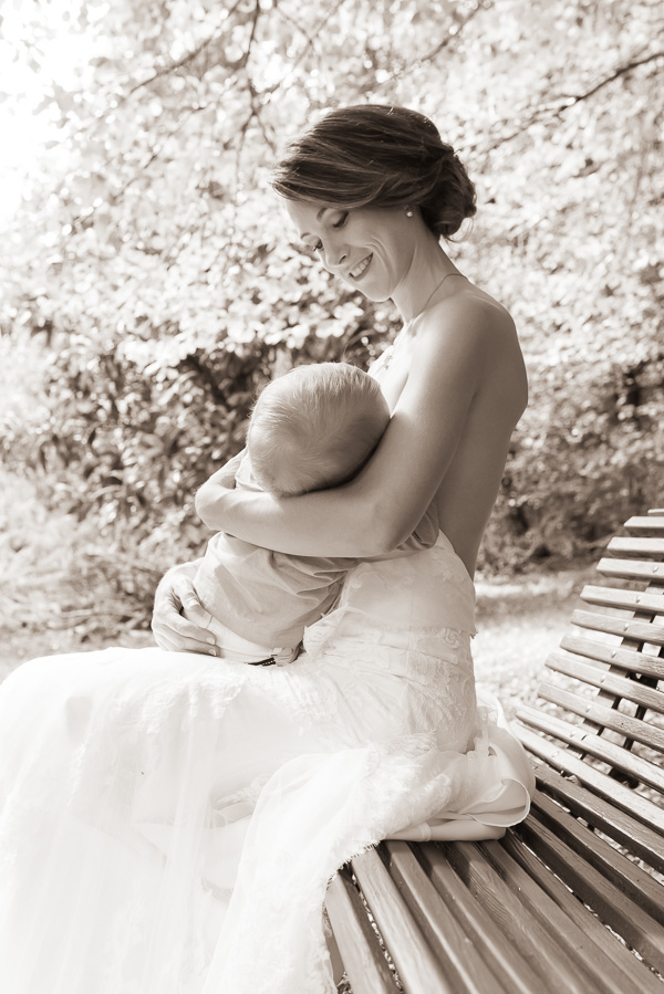 Une maman assise sur un banc en robe de mariée allaitant son bébé