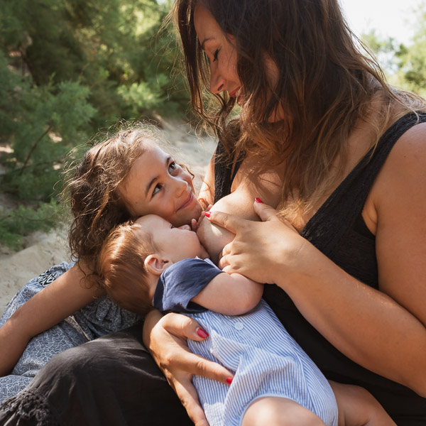 Maman allaitant son bébé entouré de ses enfants, à la plage.